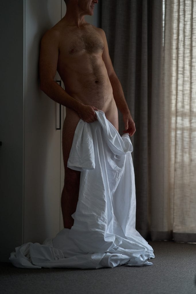 melbourne male escort standing naked with a white bedsheet covering his lower body